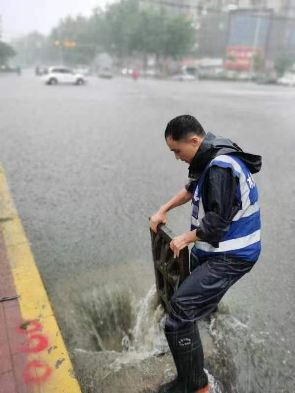 集团工作人员冒雨掀开雨水井盖加快排水